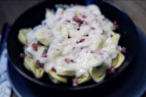 bakterienbefallende Tortellini mit Schinken angerichtet auf einem dunklen Teller