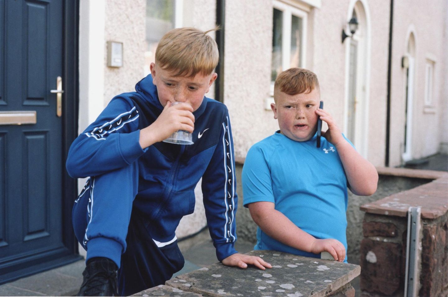 Fremd im eigenen Land Zwei Jungen stehen vor einem Haus. Einer pustet in einen Platikbecher. Einer hält ein Smartphone an sein Ohr
