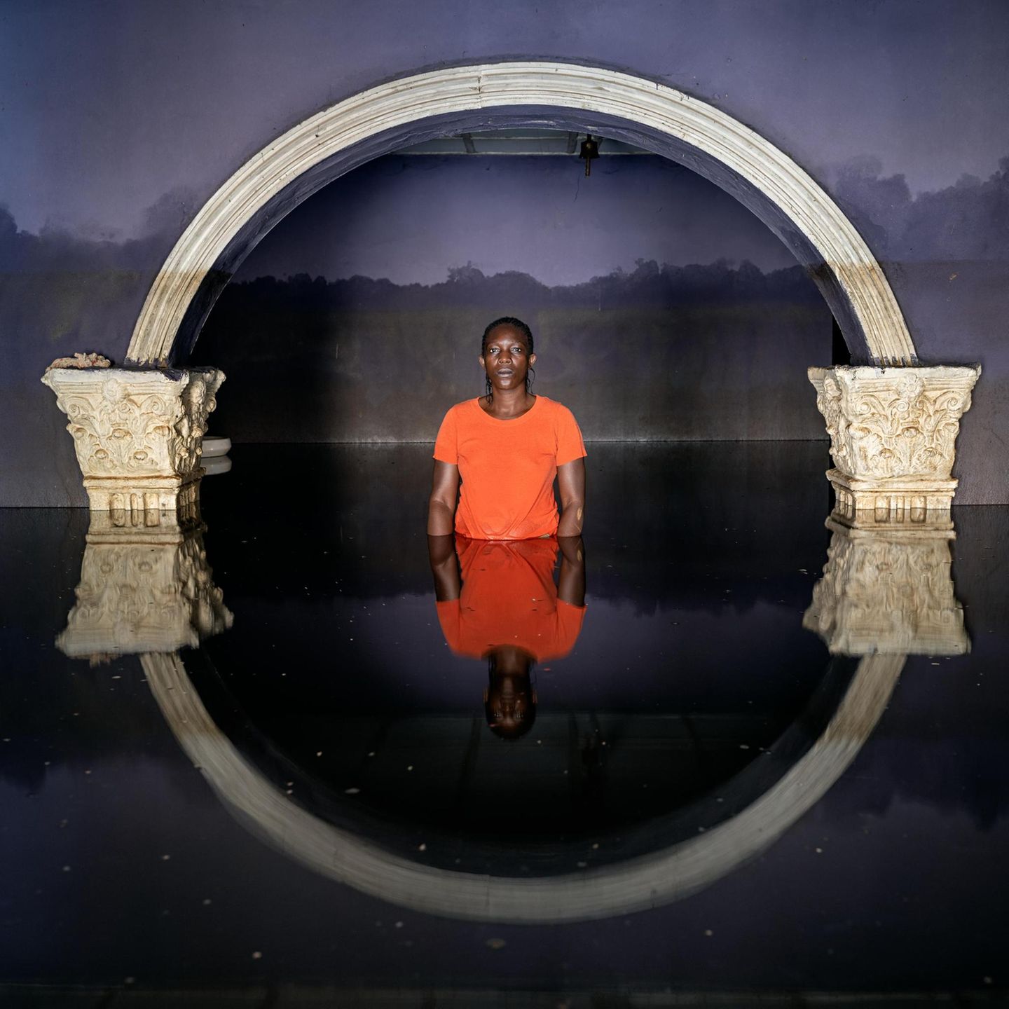 Überflutet Eine Person in roter Kleidung steht bis zur Hüfte in Wasser. Über ihr ein Torbogen, der sich in der Wasseroberfläche spiegelt
