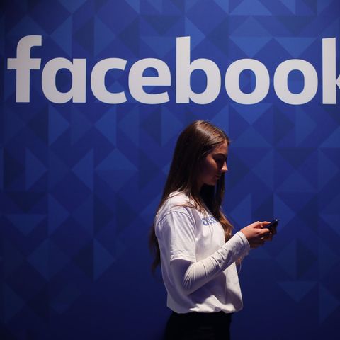 Eine Frau steht vor einem Logo der Meta-Tochter Facebook