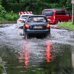 Nach starken Regenfällen und Unwettern bahnen sich Autos in Berlin ihren Weg durch eine überspülte Straße
