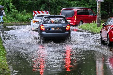 Nach starken Regenfällen und Unwettern bahnen sich Autos in Berlin ihren Weg durch eine überspülte Straße
