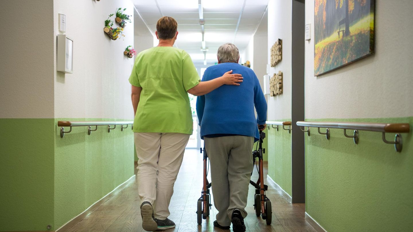 Eine Seniorin wird von einer Pflegekraft durch ein Pflegeheim geleitet