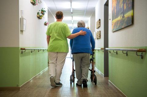 Eine Seniorin wird von einer Pflegekraft durch ein Pflegeheim geleitet