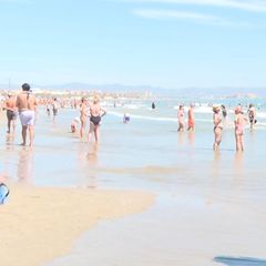 Zahlreiche Menschen stehen in Badekleidung am Strand und im Wasser in Südeuropa.