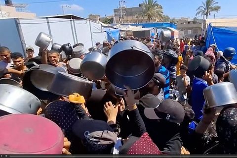 Menschen stehen in Massen an der Essensausgabe in Gaza und halten leere Töpfe in die Luft.