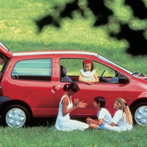 Eine Familie sitzt um einen roten Kleinwagen herum im Gras