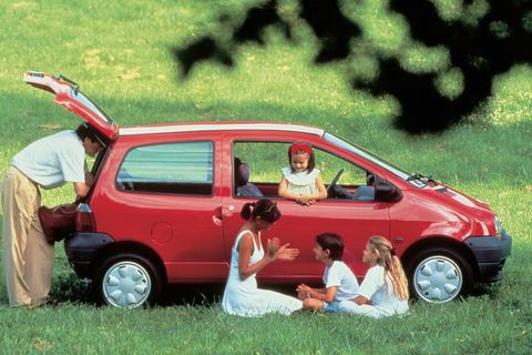 Eine Familie sitzt um einen roten Kleinwagen herum im Gras