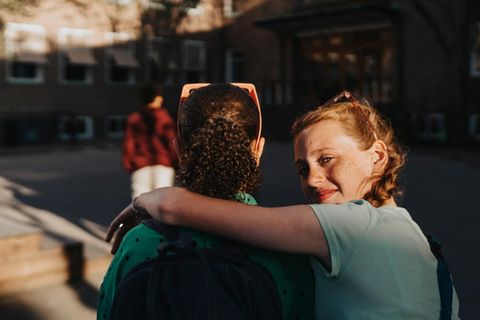 Zwei Teenie Mädchen umarmen sich vor einer Schule