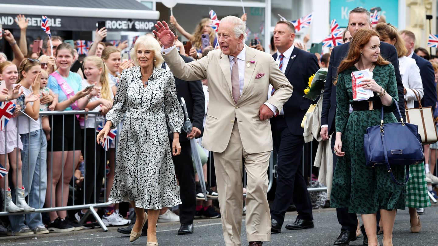 Königin Camilla und König Charles bei einem Besuch in Newmarket. Der König winkt dem Volk zu