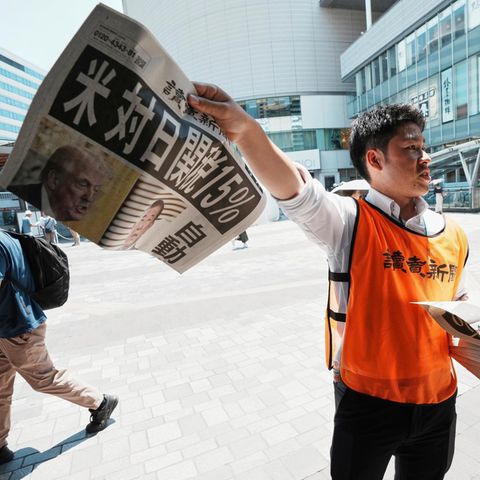 A newspaper seller with a title page for the trade deal between the USA and Japan