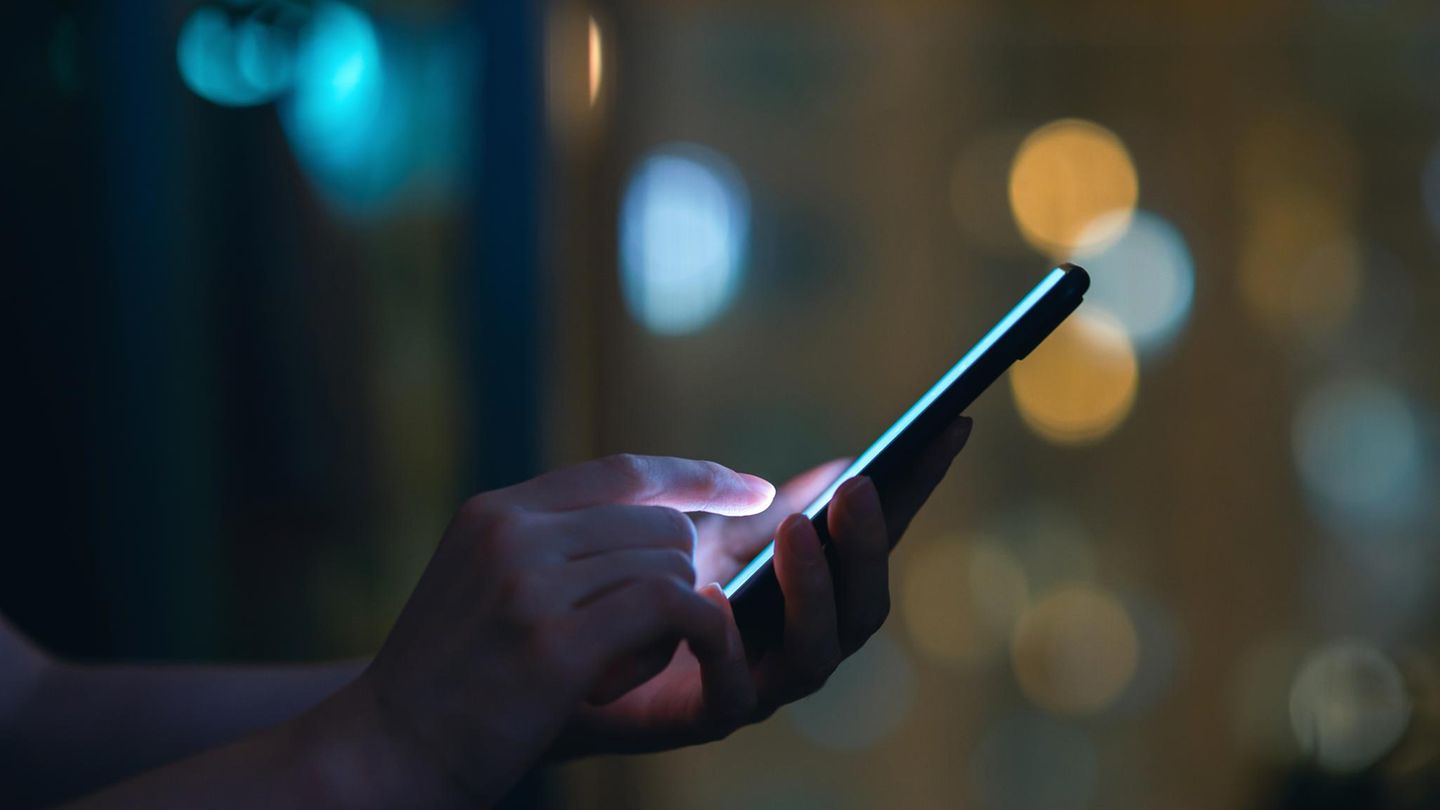 Eine Person schaut im Dunkeln auf ein leuchtendeds SMartphone und tippt SMS oder Whatsapp