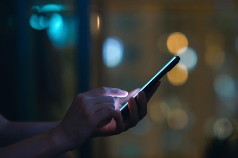 Eine Person schaut im Dunkeln auf ein leuchtendeds SMartphone und tippt SMS oder Whatsapp