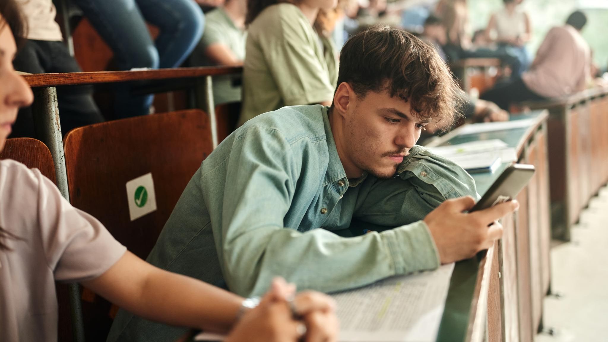 Symbolfoto Schule: Gelangweilter Schüler mit Handy im Unterricht
