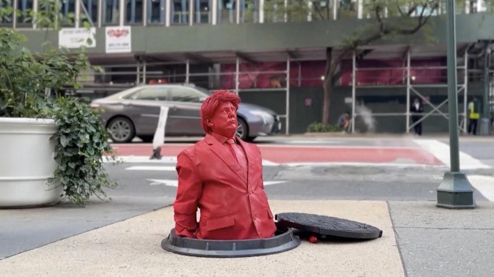 Trumps Oberkörper ragt aus einem Kanaldeckel, daneben eine Ratte
