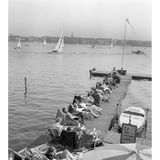 Menschen in Sonnenstühlen auf einem Steg am Wasser