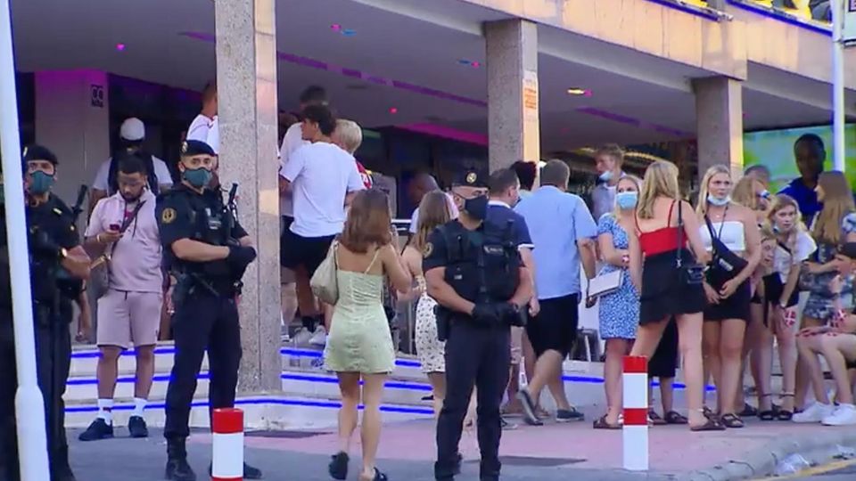 Mehrere Polizisten stehen mit Mund-Nasenschutz vor einer Menge partylustiger Menschen am Ballermann.