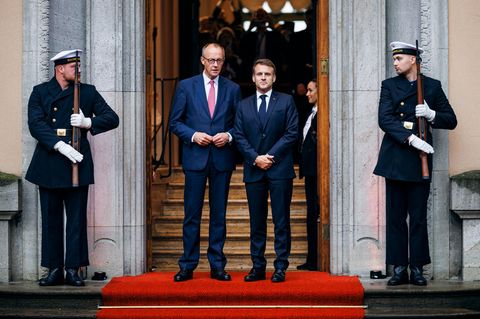 Merz und Macron stehen am einem Eingang nebeneinander und posieren