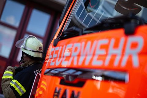 Feuerwehrauto von vorne. Daneben steht ein Feuerwehrmann mit Helm