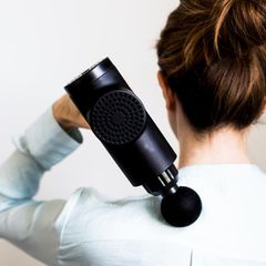 Eine Frau massiert ihren Nacken mit einem Handmassagegerät