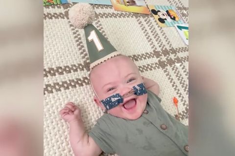 Nash trägt einen Partyhut und lacht fröhlich in die Kamera. Dazu trägt er eine Sauerstoff-Nasenbrille.