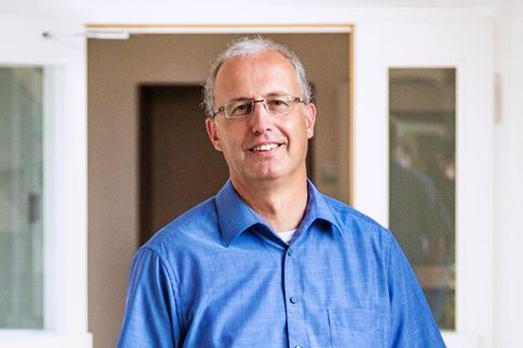 Jörg Teusch, kurzes graues Haar, eckige Brille, schaut in die Kamera. Er trägt ein blaues Hemd
