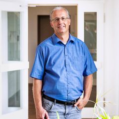Jörg Teusch, kurzes graues Haar, eckige Brille, schaut in die Kamera. Er trägt ein blaues Hemd