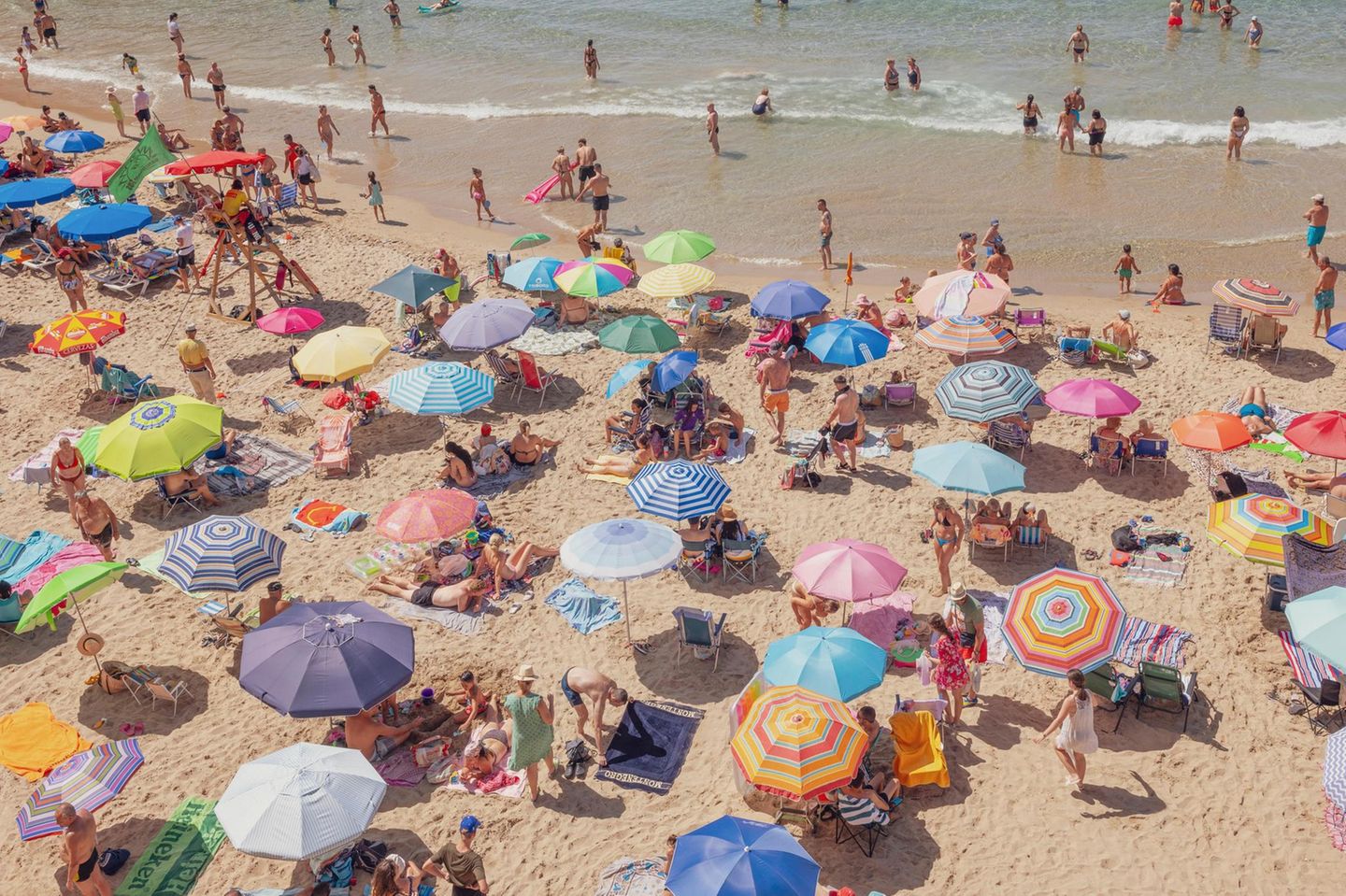 Urlauber und ihre bunten Sonnenschirme über den Strand verteilt
