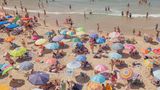Urlauber und ihre bunten Sonnenschirme über den Strand verteilt