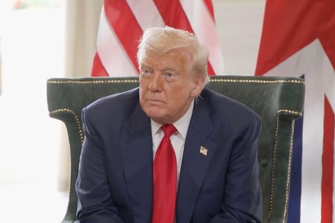 Trump sitzt auf einem Sessel und schaut nach vorne.