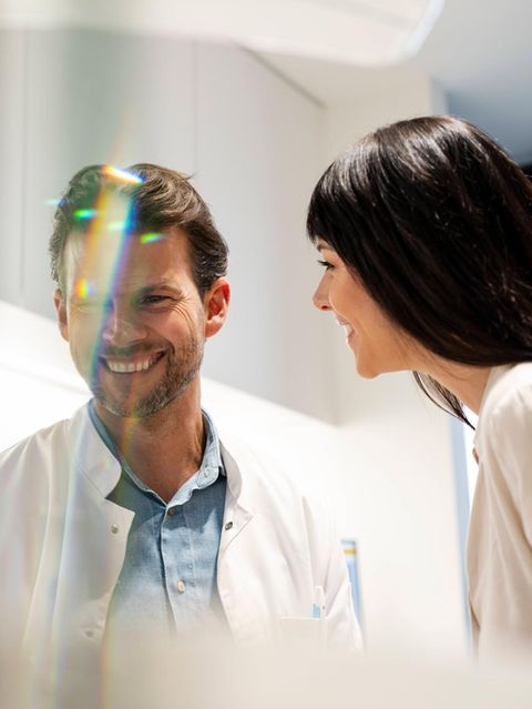 Ein Arzt im weißen Kittel lacht neben einer Patientin (Symbolbild Affäre)