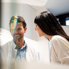 Ein Arzt im weißen Kittel lacht neben einer Patientin (Symbolbild Affäre)