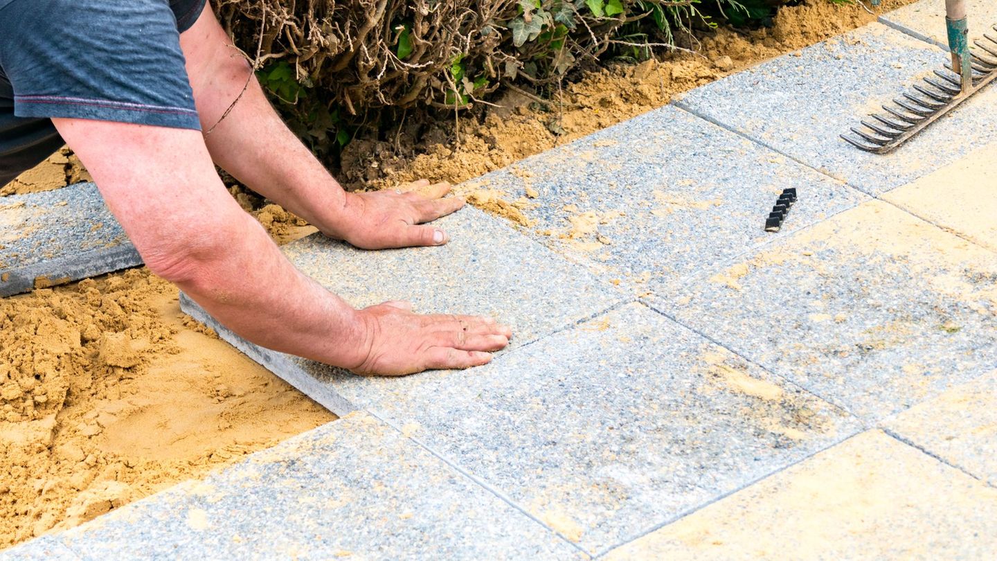 Der Maurer legt Kiesplatten auf Sand, um eine Gasse zu machen