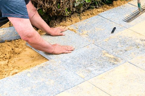 Der Maurer legt Kiesplatten auf Sand, um eine Gasse zu machen