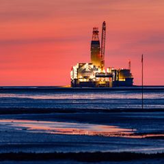 Vor leuchtend rotem Abendhimmel gibt die Ölplattform Mittelplate in der Nordsee ein romantisches Bild ab
