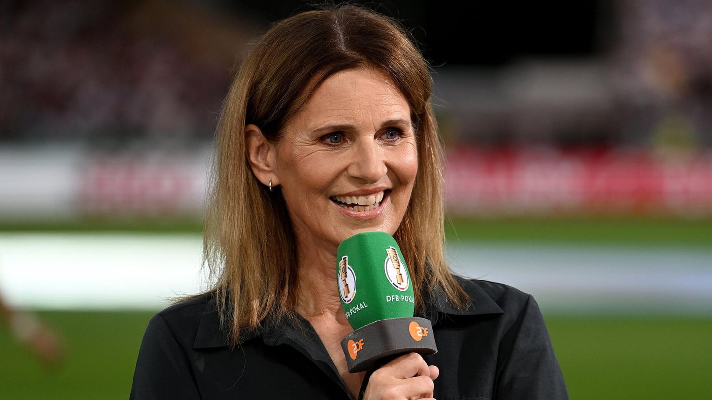 Portrait der Fersehmoderatorin Katrin Müller-Hohenstein. Sie steht auf einem Fußballfeld und hält ein Mikrofon in der Hand.