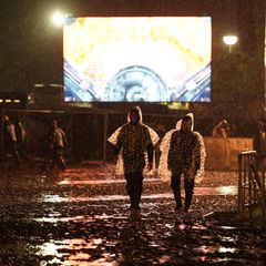 Wacken-Besucher trotten in Regen-Ponchos über das nächtliche Festivalgelände