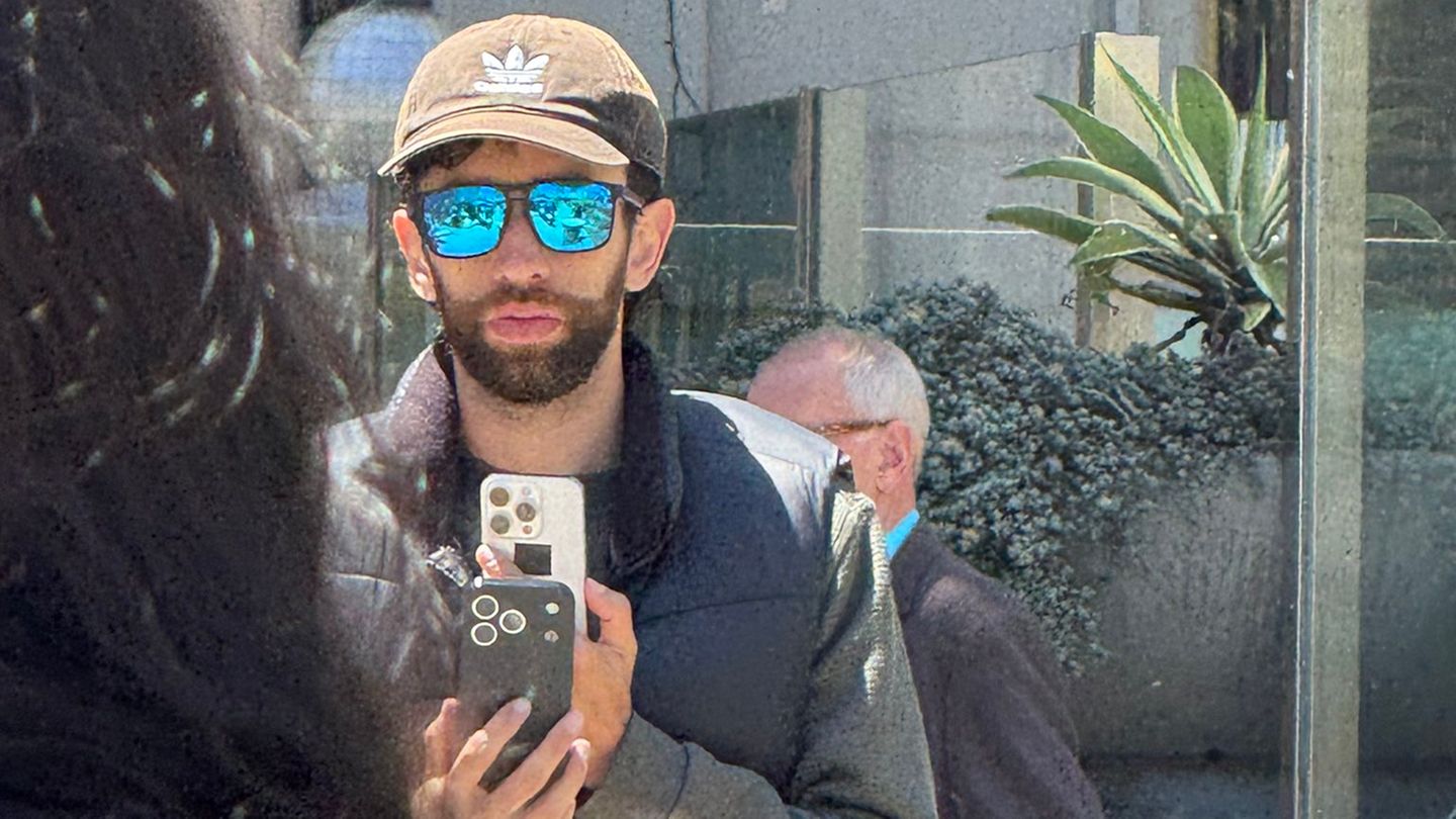 Eine Person mit Kappe und Sonnebrille hält ein iPhone in der Hand, dessen Design den Gerüchten zum iPhone 17 entspricht