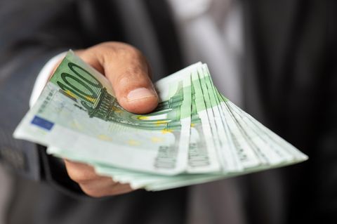 Gehalt bar vom Chef: Ein Mann reicht dem Betrachter eine Handvoll 100-Euro-Scheine