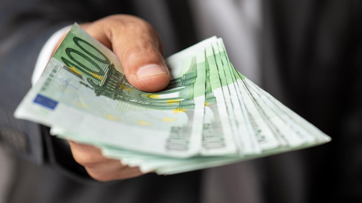 Gehalt bar vom Chef: Ein Mann reicht dem Betrachter eine Handvoll 100-Euro-Scheine