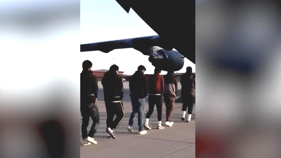 Migranten laufen in ein gefesselt in ein Flugzeug