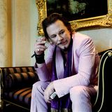 Bryan Adams – die Ausstellung: Mickey Rourke sitzt einem rosafarbenen Anzug auf einer Chaiselounge