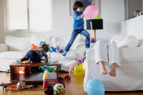 ADHS: Kinder toben durch ein Wohnzimmer, die Mutter liegt auf dem Sofa