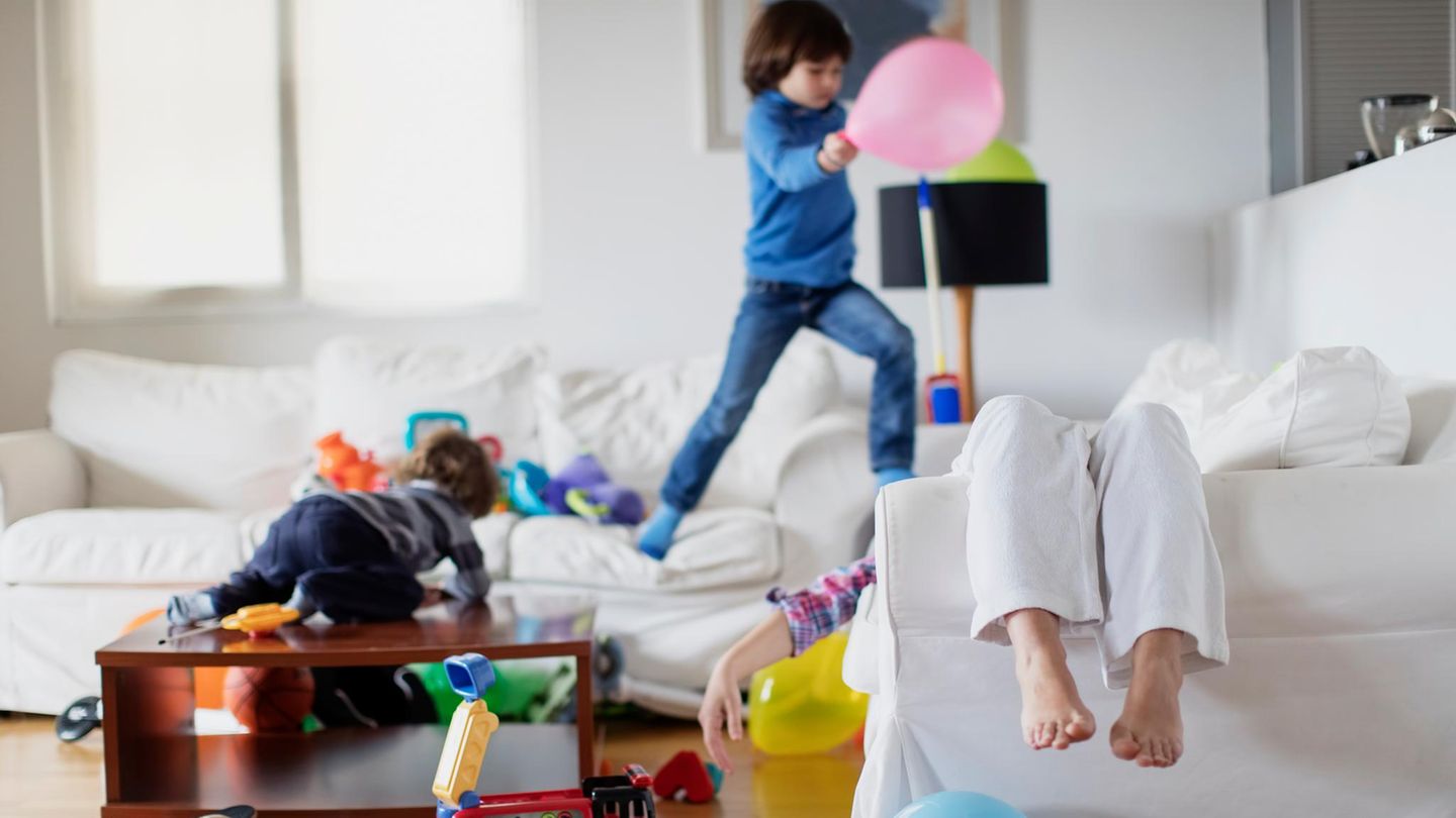 ADHS: Kinder toben durch ein Wohnzimmer, die Mutter liegt auf dem Sofa ADHS: Kinder toben durch ein Wohnzimmer, die Mutter liegt auf dem Sofa