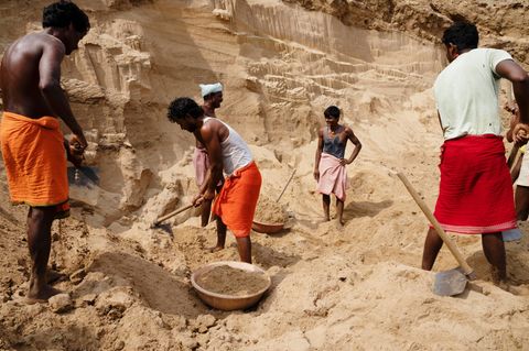 indische Arbeiter schaufeln Sand an einem Flussufer