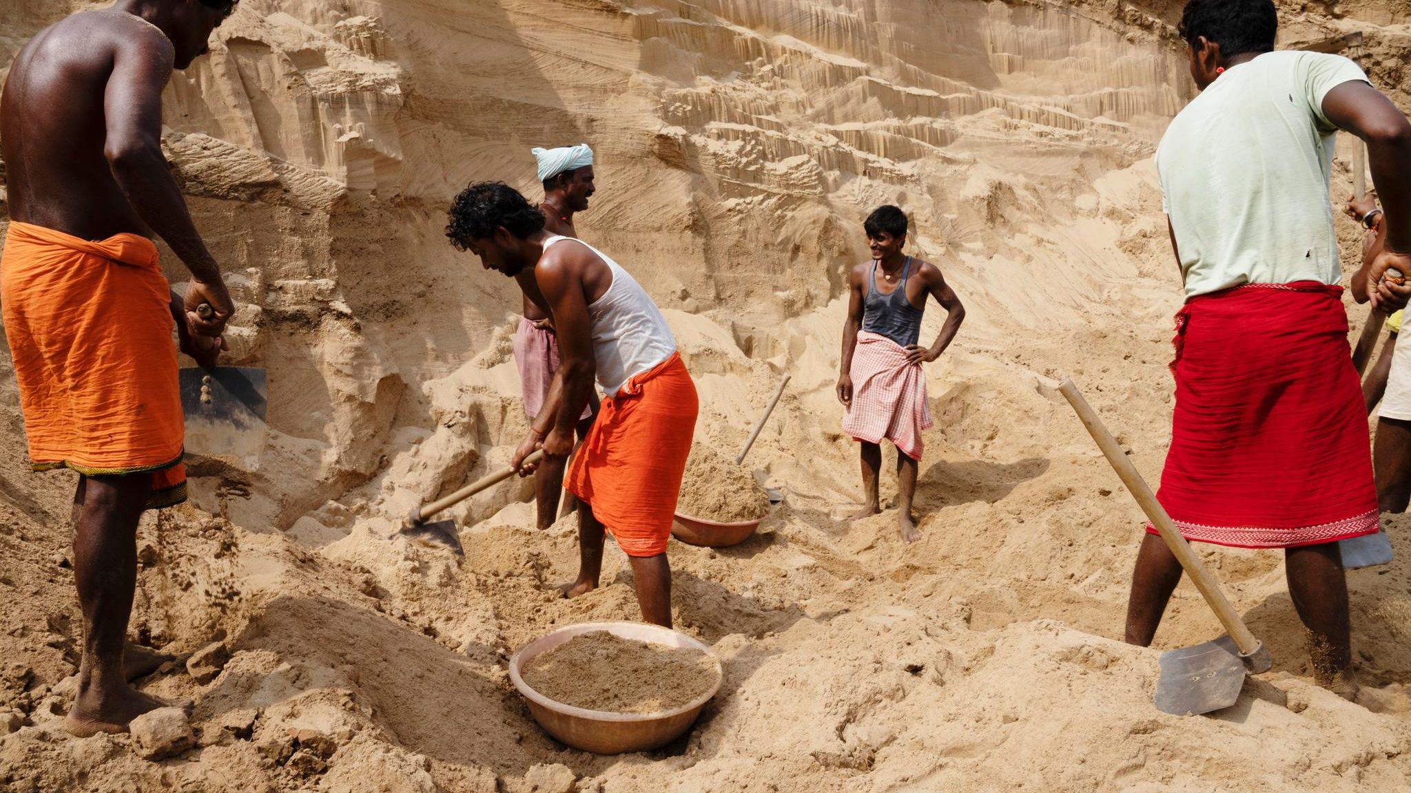 indische Arbeiter schaufeln Sand an einem Flussufer