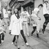 Naomi Campbell stolziert in weißem Mantel und mit weißer Sonnenbrille durch eine Gruppe von Jungen