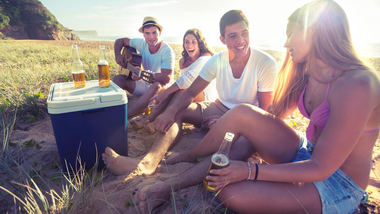 Personen sitzen beim Camping um eine Kühlbox herum