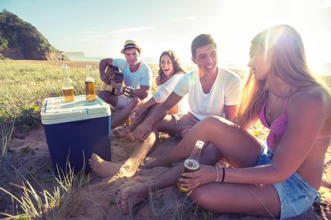 Personen sitzen beim Camping um eine Kühlbox herum