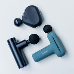 Drei Massagepistolen liegen auf einem hellen Untergrund